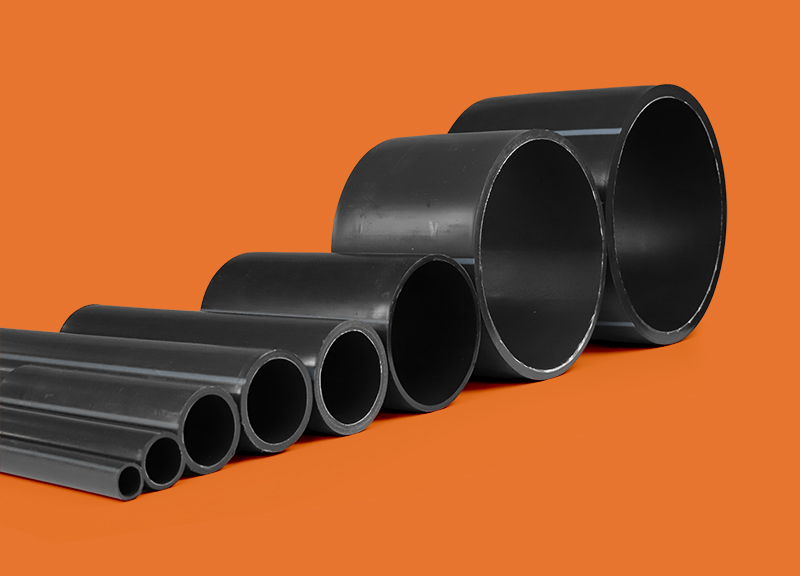 Variedade de tubos Tucano Liso em preto, com superfícies lisas e seções abertas, dispostos em diferentes tamanhos e espessuras, sobre um fundo laranja.